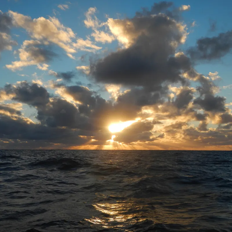 Sunset over the ocean with clouds and sun rays breaking through.